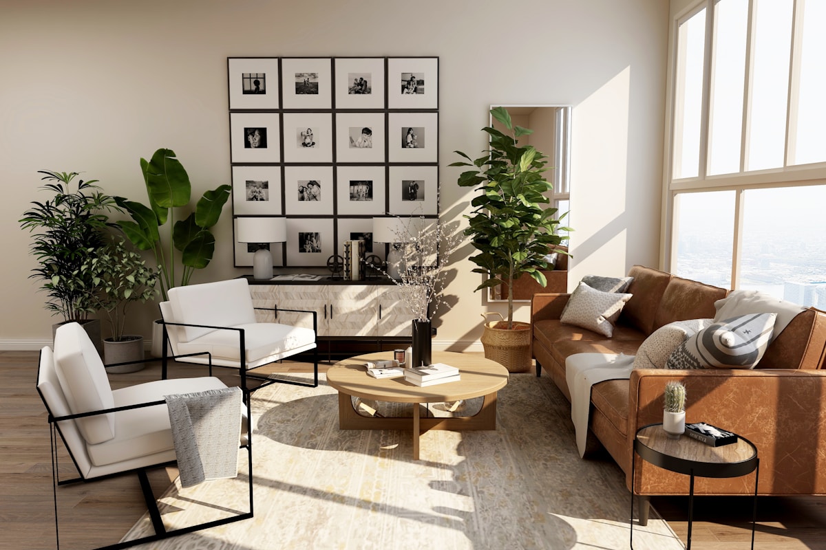 Warm modern living room with a tan leather sofa, two white chairs, round wood coffee table, large houseplants, and a grid of 16 black-and-white framed photographs above a sideboard.
