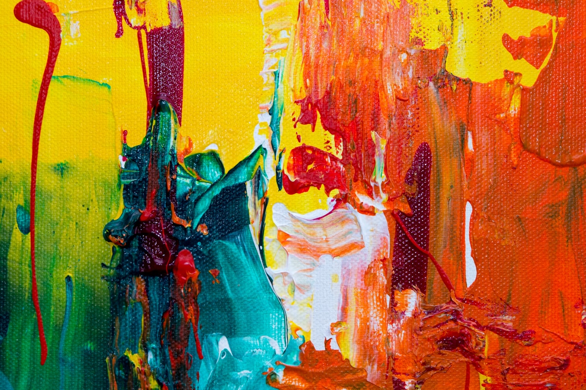 Close-up of a vibrant abstract painting with thick yellow, orange, red, teal, and white paint strokes on a textured canvas.