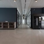 Empty modern open-plan office corridor with polished concrete floor, a glass-walled meeting room on the right, and a long wooden credenza on the left.
