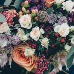 Close-up of a full floral bouquet with peach and cream garden roses, deep purple berries, pink hypericum, and eucalyptus foliage.