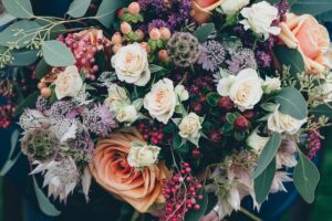 Close-up of a full floral bouquet with peach and cream garden roses, deep purple berries, pink hypericum, and eucalyptus foliage.